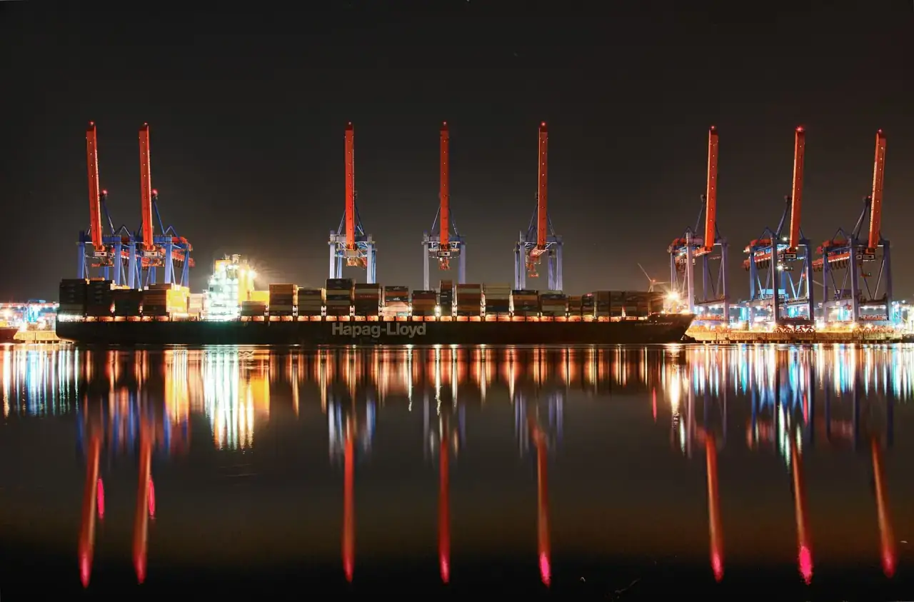 Container terminal gantries lit at night beside a berthed container ship.